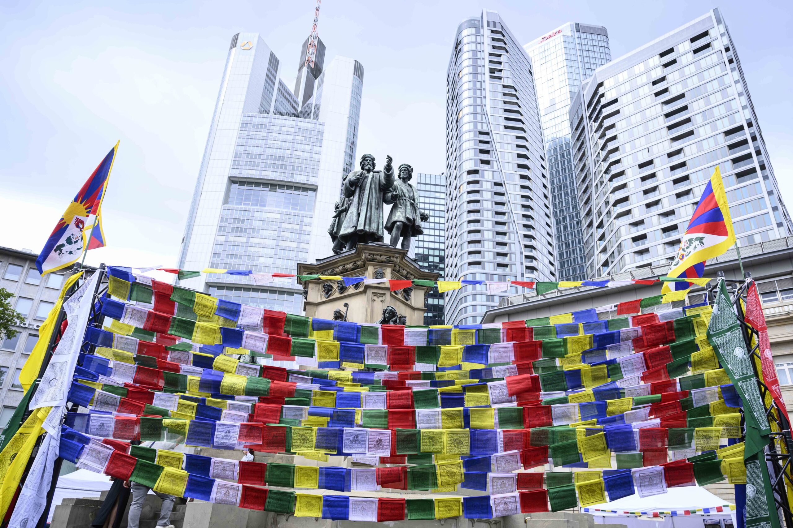 Tibetische Gebetsfahnen vor Hochhäusern. Tibet Fest | Tibet Haus, aufgenommen am Samstag (23.08.2025) auf dem Roßmarkt in Frankfurt am Main. Foto: Salome Roessler / lensandlight
