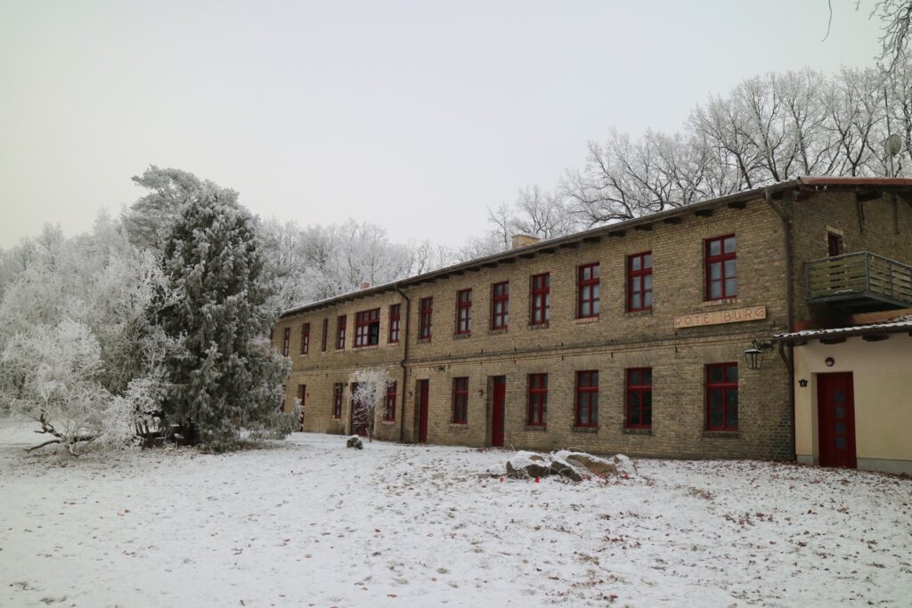 Das neue Retreatzentrum, die "Rote Burg". Ein einstöckiger, gelblicher Ziegelbau mit rot gestrichenen Fenstern mit Fenstersprossen. 